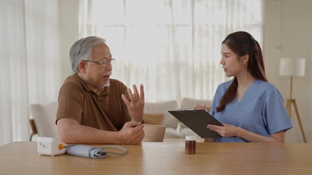 Elderly patient and senior man discussing healthcare with nurse during home medical consultation, reviewing wellness information beside blood pressure monitor and medicine container bright living