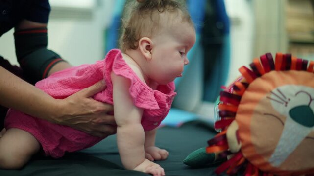 Infant girl with red hair in a pink shirt playing with a soft lion toy during an early developmental therapy session