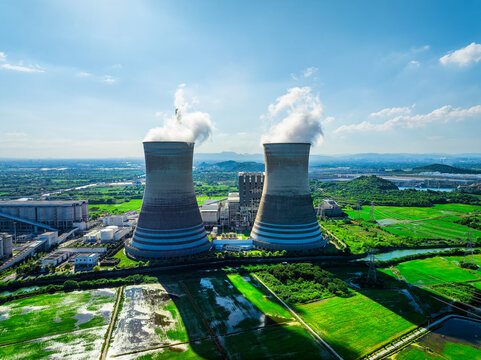 Industrial power plant with steaming cooling towers beside irrigated farmland and green agricultural fields, highlighting energy infrastructure and rural development.