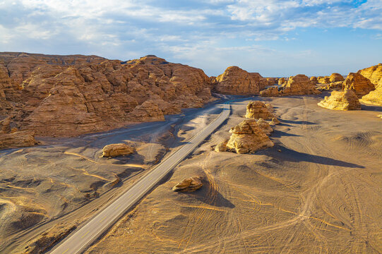 Aerial view of asphalt road winding through Dahaidao yardang landforms in Xinjiang desert during the day.