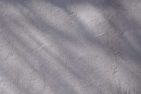 close-up view of a weathered gray concrete surface with subtle variations in tone and rough texture. Soft natural lighting highlights the uneven plaster, fine imperfections, stains, and aged areas acr