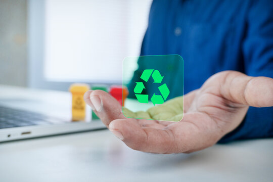 Person holding open hand with green recycling symbol hologram graphic and small recycling bins on desk, concept of environmental sustainability, zero waste, circular economy, and green technology.