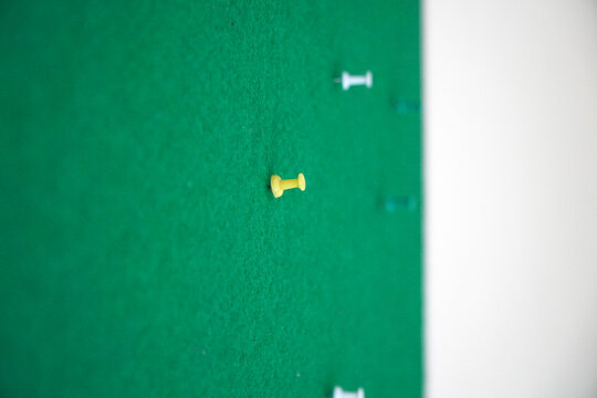 Red and yellow push pin stuck on a green felt notice board with selective focus and copy space. Concept for reminder, target, location marking, office organization, and business planning.