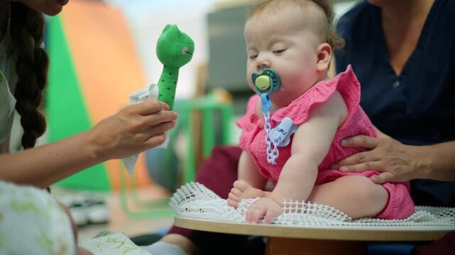 Baby girl sitting on a support, receiving early intervention and physical therapy with a therapist stimulating her with a toy