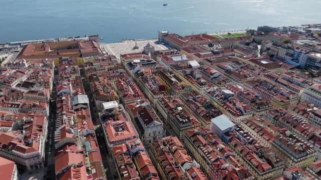 Stunning drone shot above Lisbon&rsquo;s Baixa district, capturing iconic Portuguese architecture, red-tiled roofs, Praca do Comercio, and sparkling Tagus River in crisp daylight aerial footage.