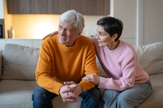 Caring wife consoling distressed husband on sofa, compassion and family support in life problems, understanding woman embracing stressed unhappy man, empathy in crisis, dealing with difficulties.