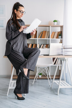 Paperwork routine. Business manager. Serious woman specialist reviewing document at desk with laptop at modern professional workplace.