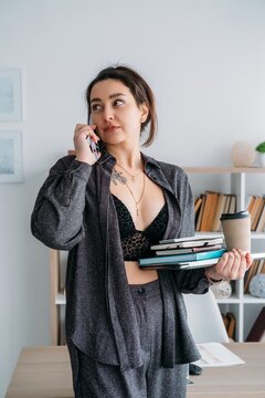 Office manager. Digital workflow. Female talking on smartphone with notebook coffee using laptop preparing for business paperwork.