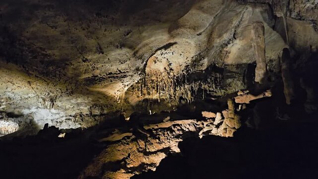 Ancient limestone cavern with rough rock floor, stalagmites rising from the ground, stalactites overhead, cool cave lighting, dark shadows, and scenic underground formations.