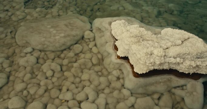 Top down view of thick white Dead Sea salt crystals covering a submerged rock beneath clear mineral rich water in Jordan, showcasing natural salt formations and unique geological patterns