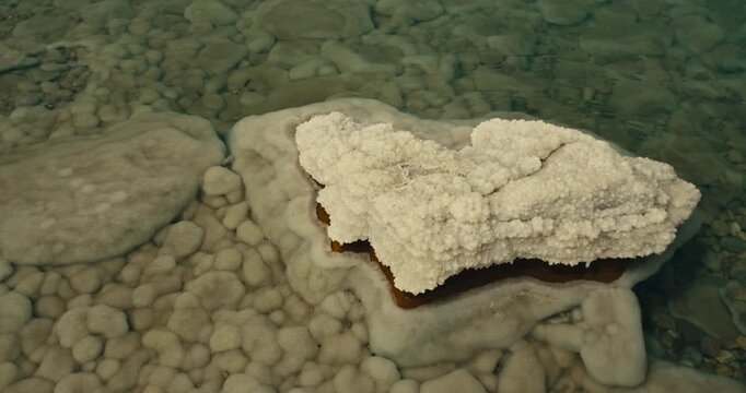 Close up of a thick layer of Dead Sea salt crystals covering a mineral rock beneath clear shallow water in Jordan, showcasing natural crystallisation and unique geological formations