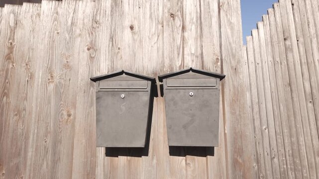 Two metal mailboxes mounted on wooden fence outside residential property