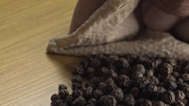 Extreme macro close up of whole black peppercorns scattered on a wooden table, highlighting rich texture, natural appearance and aromatic spice used in cooking and seasoning