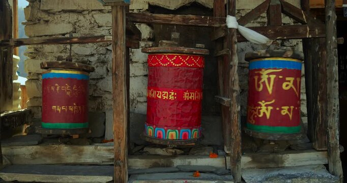 Annapurna Circuit, Manang, Nepal, traditional hand-painted Buddhist prayer wheels set in a wooden frame against a stone wall