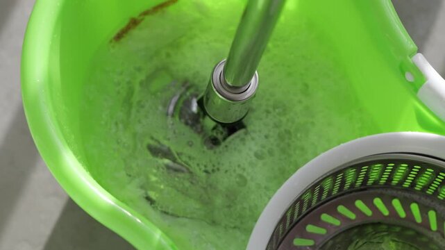 Close-up of a spin mop rotating inside a green bucket, removing excess water and preparing for efficient household floor cleaning.