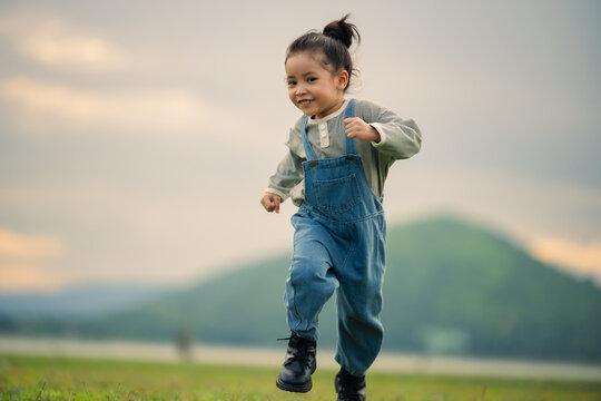 happy preschool child girl running on a grass field near river