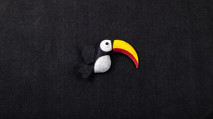 Handmade felt toucan bird decor against a black background with copy space © nilanka