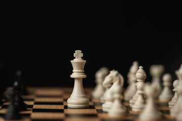 white chess king standing tall on a board, surrounded by blurred pieces on black background © geargodz