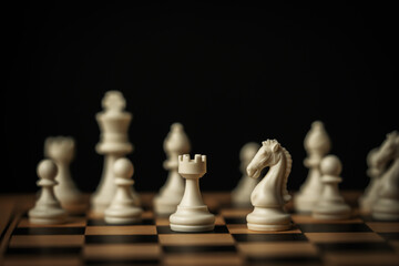 white chess knight and rook on a wooden board with other pieces on black background © geargodz
