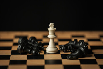 white chess king surrounded by fallen black pieces on wooden board © geargodz