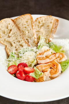 Close-up shrimp Caesar salad with toasted bread, juicy prawns, crisp greens, tomatoes and shaved parmesan on a white plate