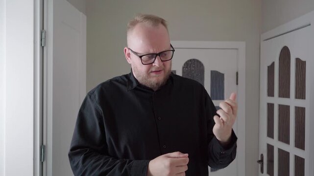 Middle-aged man in black shirt indoors examines his numb fingers and rubs his hand, acting out carpal tunnel discomfort and concern.