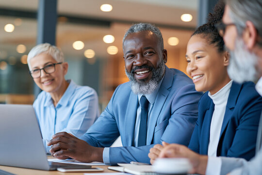 Diverse group smiles during collaborative meeting. Laptop sits center as discussion unfolds. Warm lighting highlights professional camaraderie. Confident expressions convey teamwork and positivity