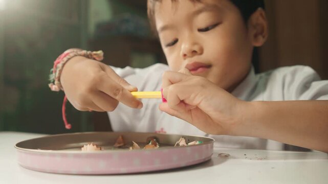 Close-up of a young child independently sharpening a colored pencil, practicing hand coordination, finger strength, concentration, and self-care skills.