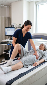 Smiling technologist positioning senior female patient on medical scanner table.