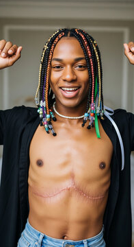 Smiling young black man with colorful braids and visible chest scar posing with arms raised wearing open shirt indoors