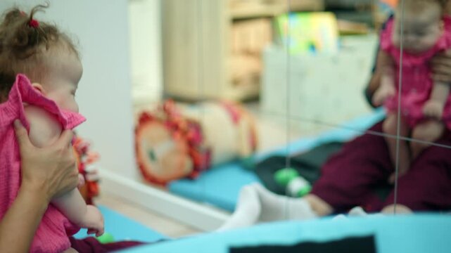 Baby girl being held while looking at her reflection in a large mirror, exploring self awareness and childhood development