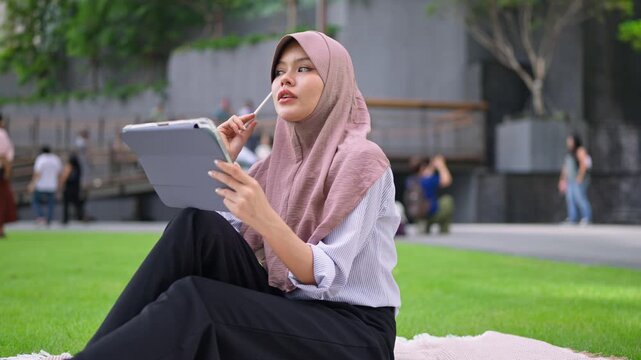 Asian young Muslim woman using a digital tablet outdoors in the city. 