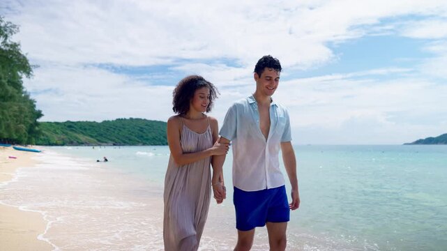 Caucasian young man and Latina girlfriend walking on sandy beach together. 