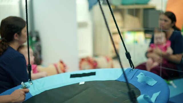 Therapist preparing a sensory swing for a baby performing early intervention exercises in a blurry clinic background