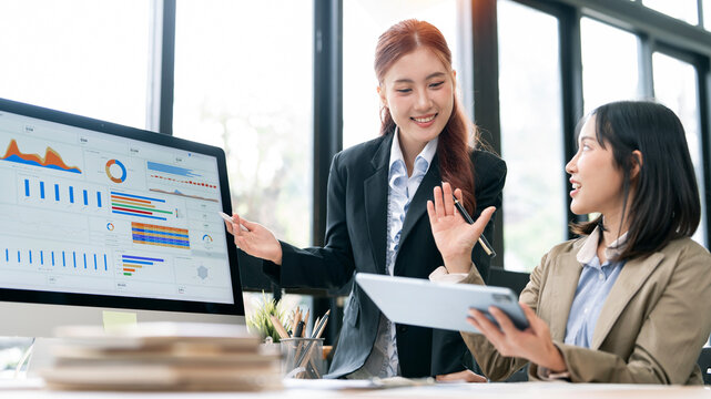 Asian Business Women Gesturing and Analyzing Charts on Computer and Tablet in Office
