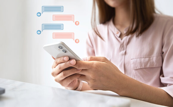 Woman using smartphone with AI chatbot speech bubble icons floating, representing customer support, digital communication and virtual assistant technology concept.