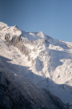 Snow blankets the peaks of mountains under a clear blue sky in the late afternoon hours