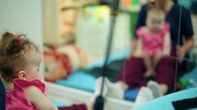 Baby girl with curly hair and pink dress observing her reflection in a mirror, developing self awareness and curiosity