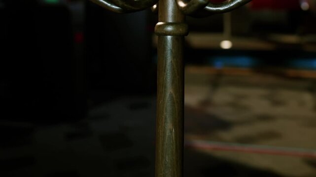 A metal coat rack occupies a corner of a dim room. The lighting creates shadows and highlights the design of the floor. It seems to be a gathering space often used for events.