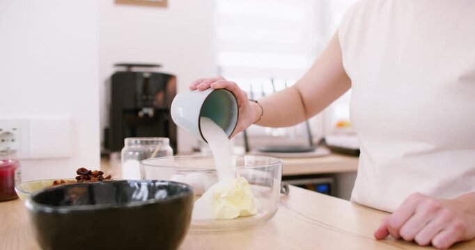 Culinary recipe. Adding sugar. Female chef hand pouring measuring sweet ingredient in glass bowl with white cream butter mass dough.