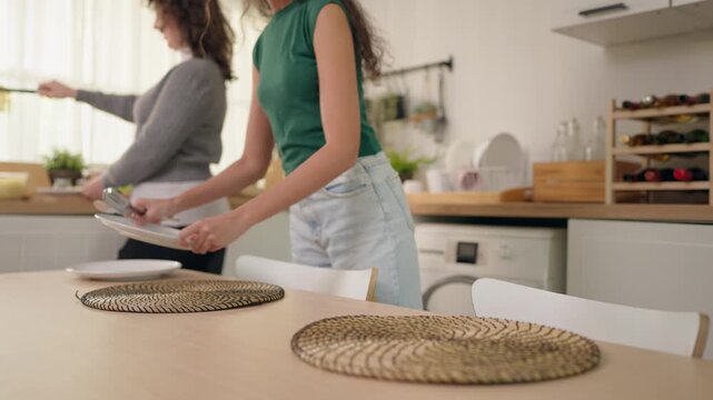 Close up of mother and young adult daughter setting the dining table. 