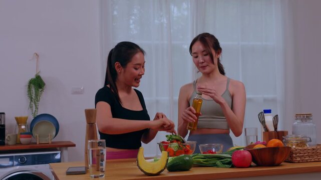 Asian woman in kitchen cooking vegetable fruit salad for healthy food preparation at home, two friends preparing fresh meal together in bright modern interior with calm smile