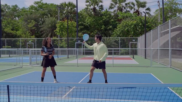 Young man and woman playing mixed doubles pickleball on outdoor court. 