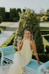 Naklejka premium Elegant woman enjoying a glass of wine in a lush garden setting