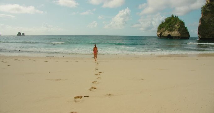 Woman walks toward the blue ocean leaving footprints in the sand at Diamond Beach Nusa Penida Bali