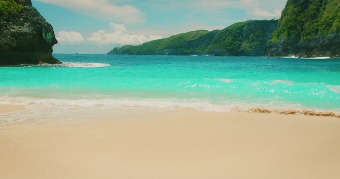 Foamy white waves washing over white sand beach near limestone cliffs in Nusa Penida