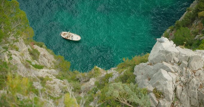 Small boat and seagull beneath steep rocky cliff above calm turquoise sea in Capri Island Italy