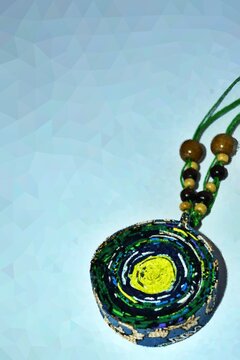 Digitally processed photo illustration of a handmade round ethnic pendant necklace with abstract green and yellow patterns on a string. Unique artisan fashion jewelry design concept.