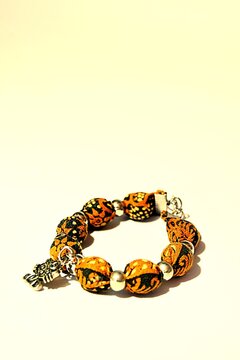 Digitally stylized photo illustration of a handmade ethnic bracelet with orange batik fabric beads and a silver charm. Perfect for fashion, cultural crafts, and artisan jewelry design concepts.