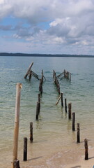 A close-up view of weathered wooden pier ruins standing in shallow coastal waters near a sandy shore, capturing rustic marine architecture and decay themes. © Rama